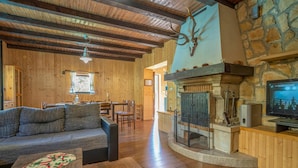 A cozy living room with a stone fireplace, wooden ceiling beams, and a television displaying a boxing match.