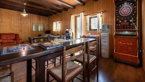 A cozy room with wooden walls and ceiling, a dartboard, a table with chairs, and a sofa.