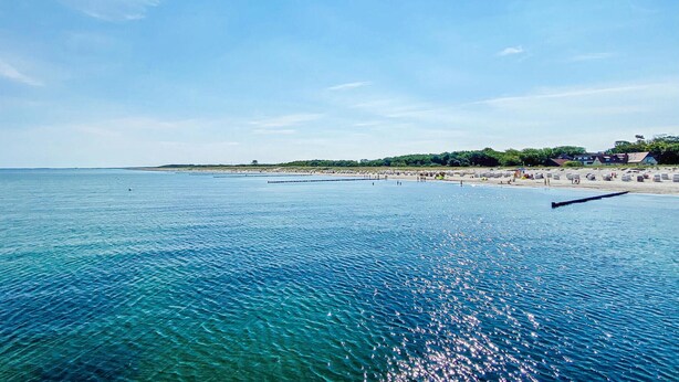 Paesaggio costiero con spiaggia, acque blu cristalline e edifici sullo sfondo.