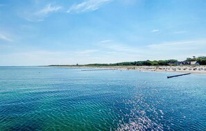 Eine Küstenlandschaft mit klarem, blauem Wasser, sandigem Ufer und Gebäuden im Hintergrund.
