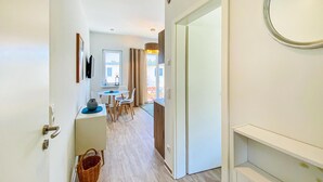 Un corridoio che conduce a una sala da pranzo con tavolo e sedie, un cesto sul pavimento e una porta con uno specchio appeso.