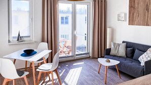Un soggiorno moderno con divano, tavolo da pranzo con sedie, balcone con tavolo e sedie e una grande finestra con tende.