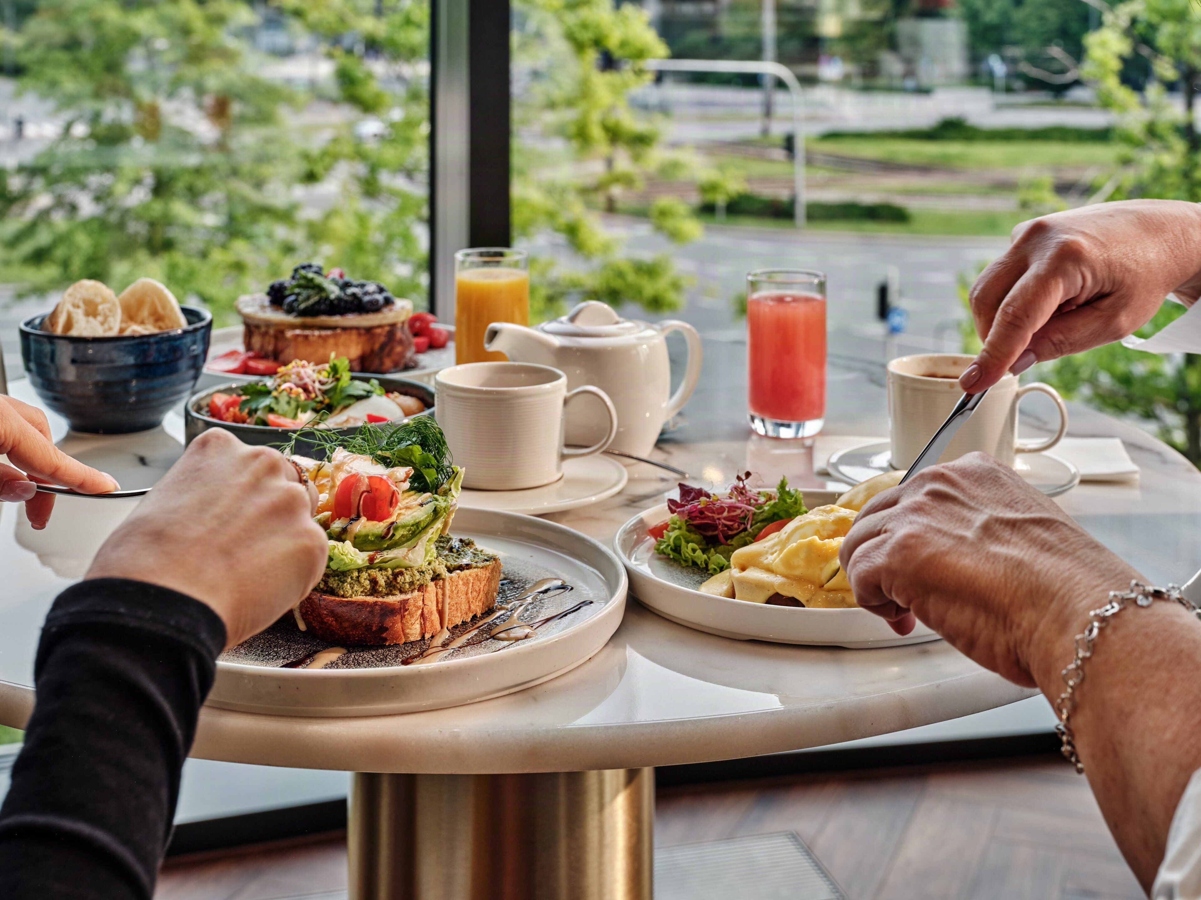 A breakfast setting with a variety of dishes, including toast with greens, a salad, and a fruit bowl. There are cups and a glass of juice on the table.