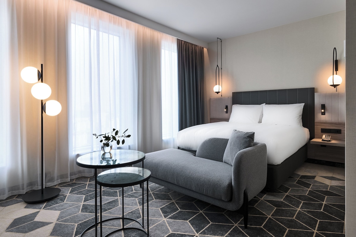 Een moderne hotelkamer met een groot bed, een slaapbank, een glazen tafel en een vloerlamp.