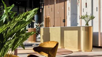A modern interior with a reception desk, seating area, and indoor plants.