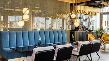 A modern bar area with a blue upholstered booth, black and grey chairs, and a bar counter with various bottles.