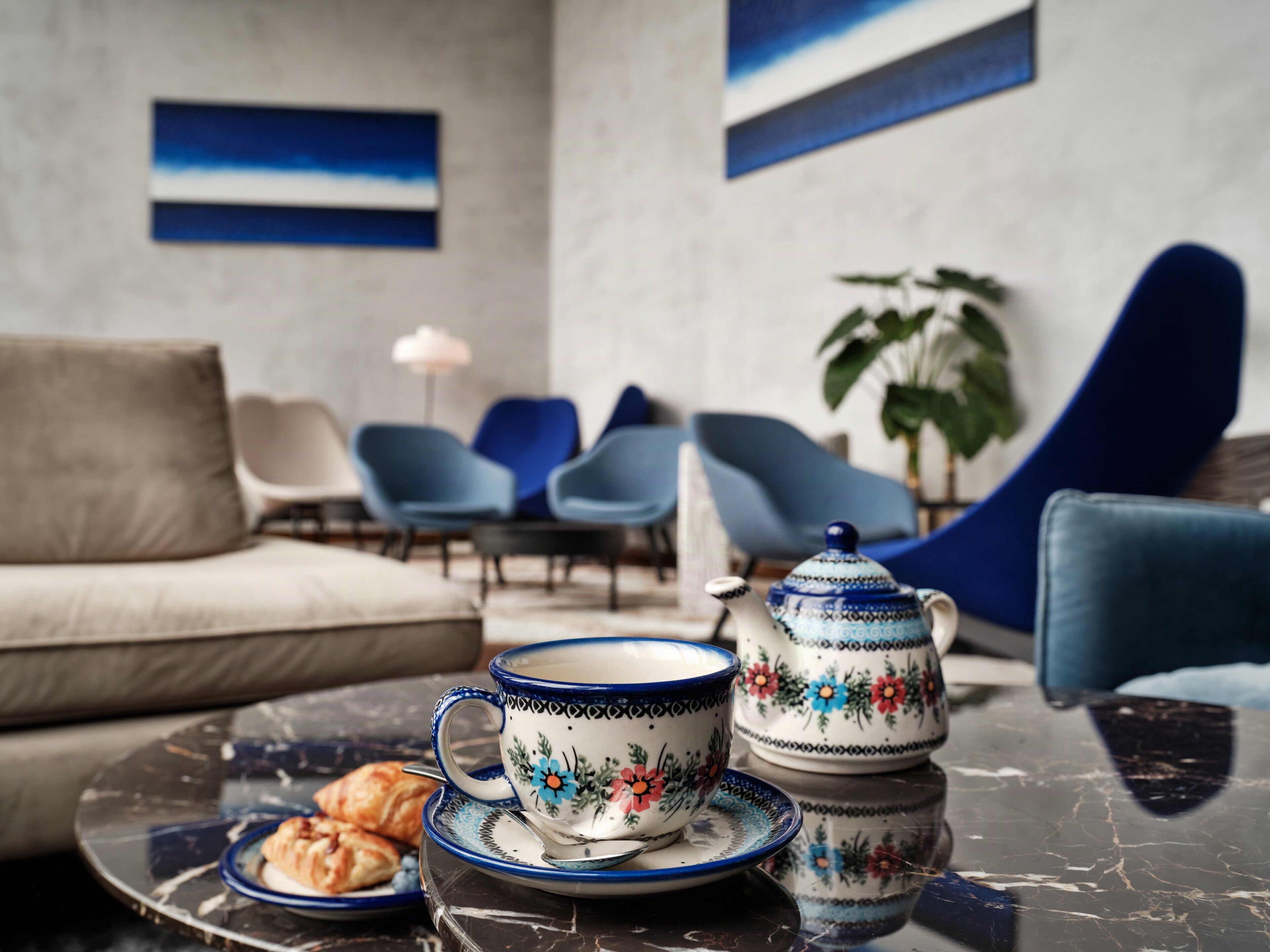 A modern living room with a sofa, chairs, a table with a teapot, cup, and pastries.
