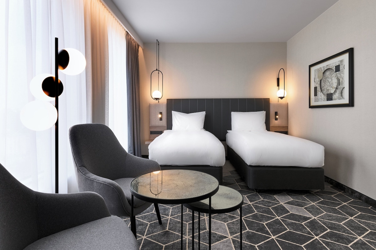 Een hotelkamer met twee bedden, een bank, een tafeltje en een lamp.