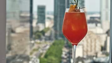 A cocktail glass with a garnish on a table, with a cityscape view in the background.