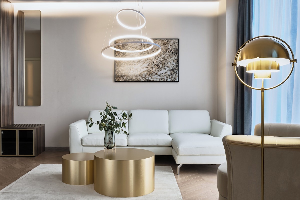 Een moderne woonkamer met een witte bank, een bolle vloerlamp en een schilderij aan de muur.