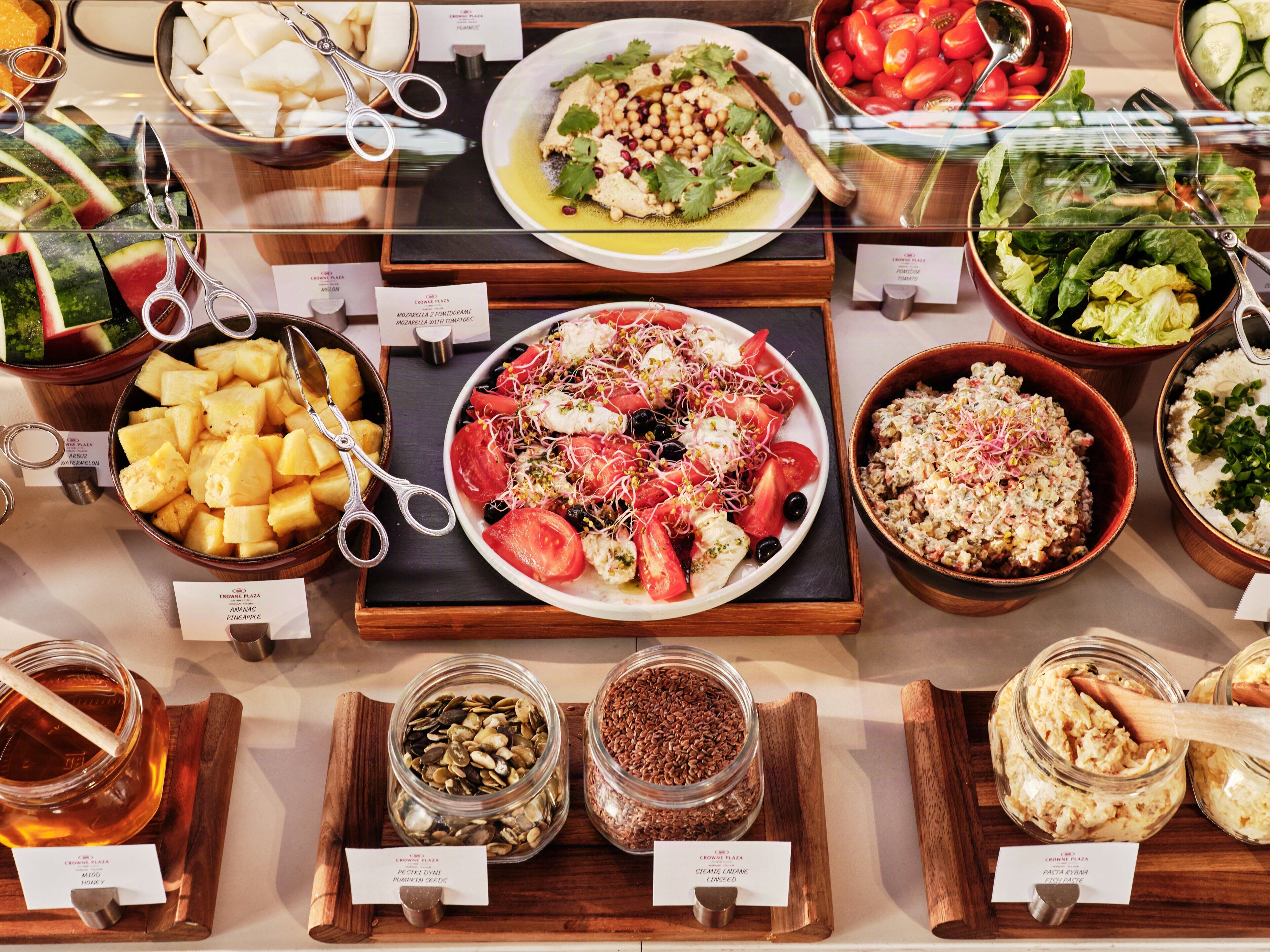 A buffet with various dishes including a plate of pasta salad, a bowl of fruit, and several jars of condiments.