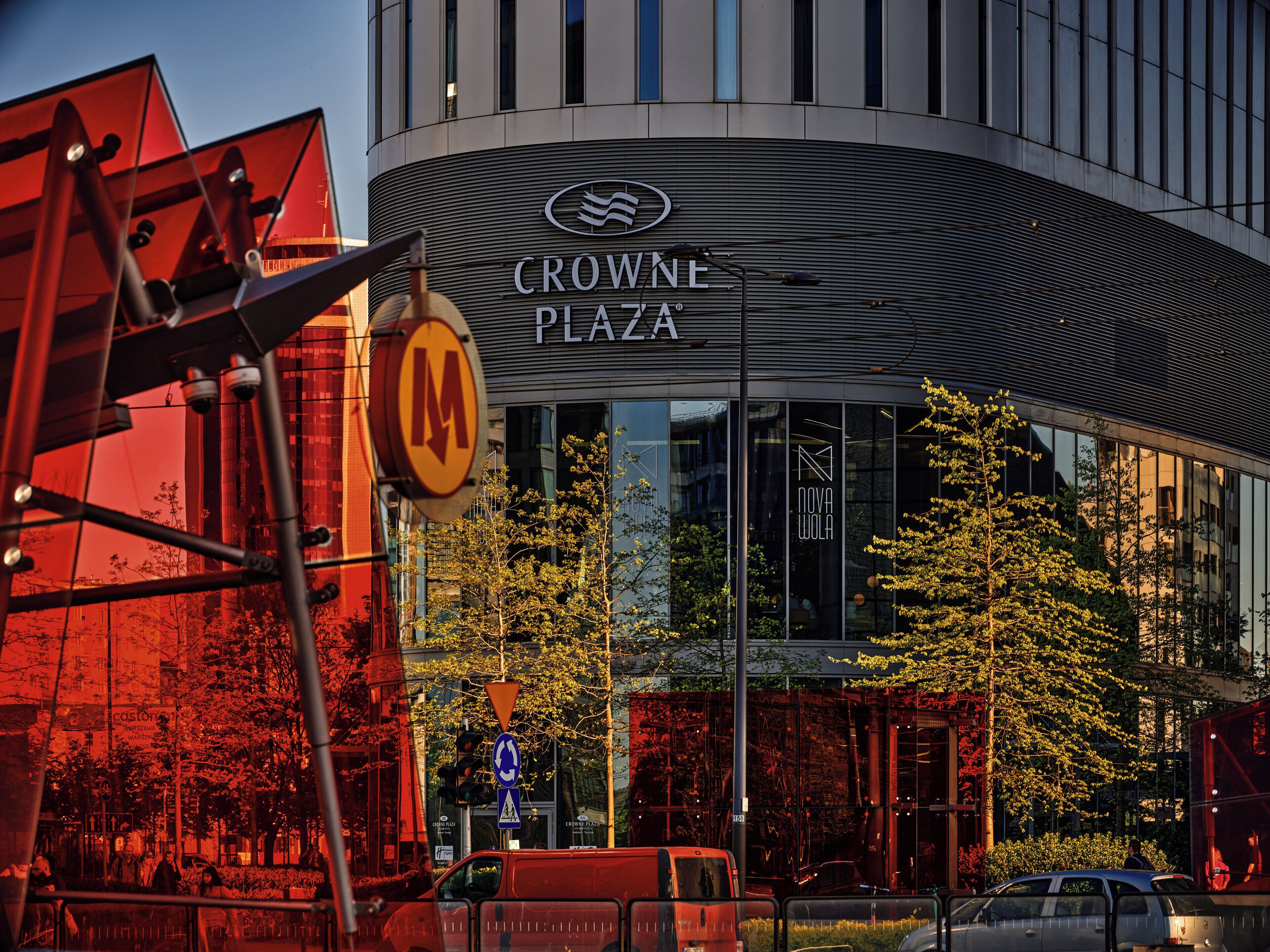 A modern building with a curved facade, a prominent 'CROWNE PLAZA' sign, and a glass entrance reflecting the surrounding trees.