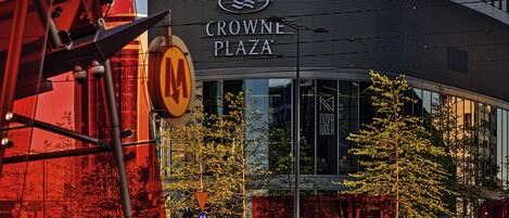 A modern building with a curved facade, a prominent 'CROWNE PLAZA' sign, and a glass entrance reflecting the surrounding trees.
