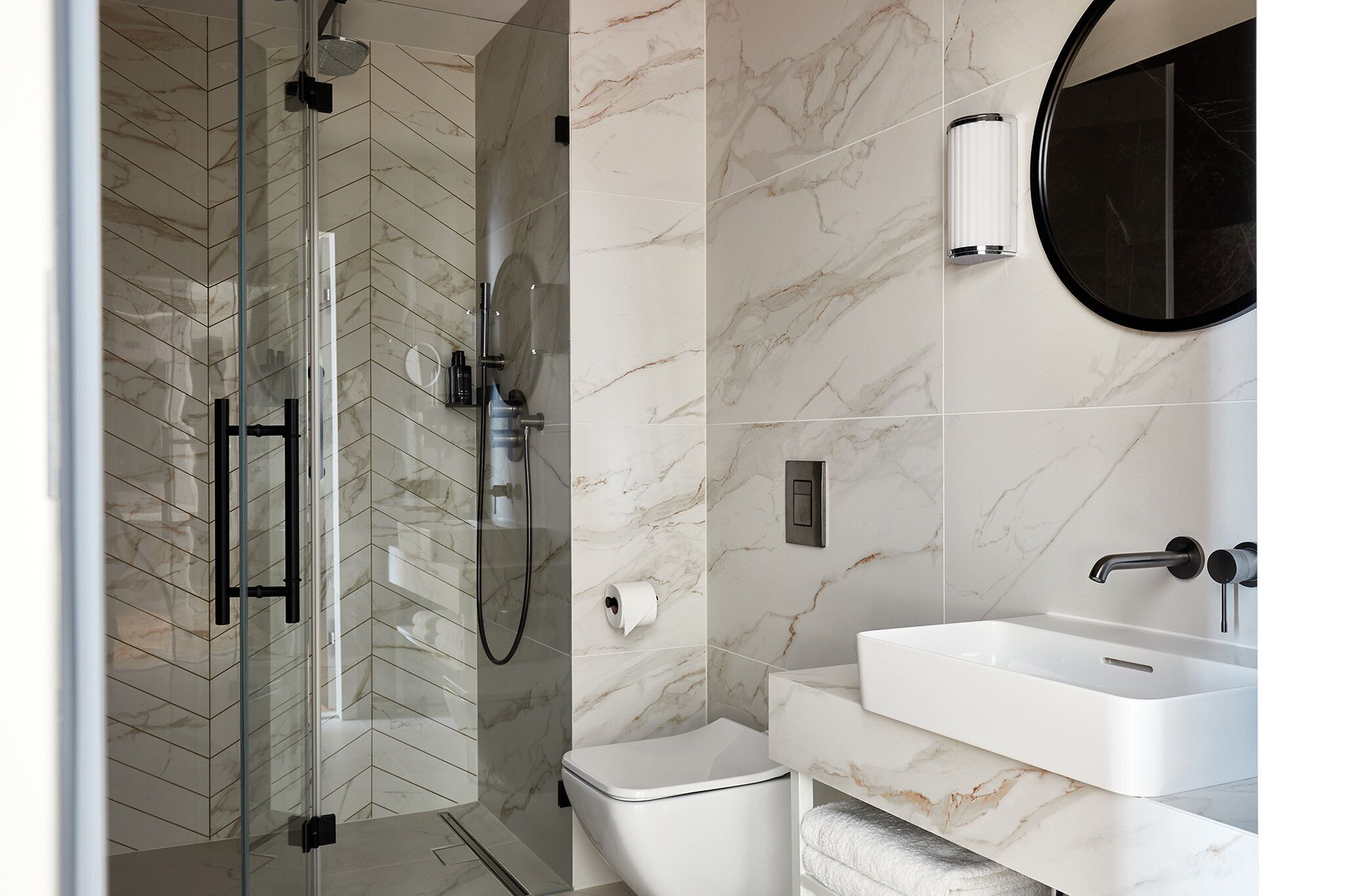 A modern bathroom with a glass-enclosed shower, a white sink, and a marble-tiled wall.
