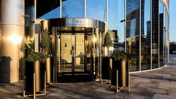 Fachada moderna de edificio con puerta giratoria, paredes de cristal y plantas en macetas.