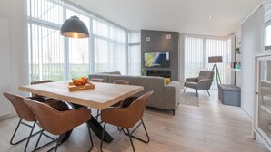 Un soggiorno moderno con zona pranzo, ampie finestre, una TV a schermo piatto e un divano grigio.