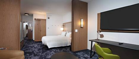 Habitación de hotel con cama, escritorio, silla y una pantalla grande.