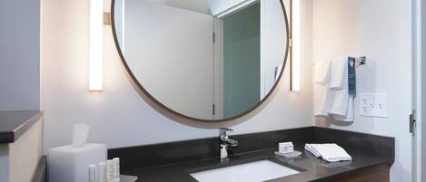 Een moderne badkamer met een ronde spiegel, een witte wastafel en een donker aanrecht.