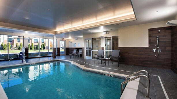 Una piscina interior con agua cristalina, una escalera metálica y una zona de estar con sillas.