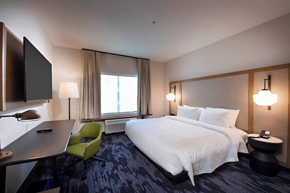 Habitación de hotel con una cama grande, un escritorio con silla, televisión y ventana con cortinas.
