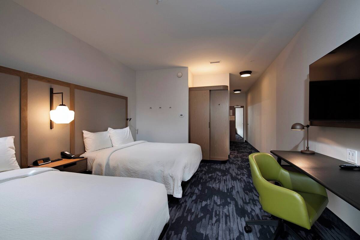 Une chambre d’hôtel avec deux lits, un bureau, une chaise verte et un téléviseur à écran plat.