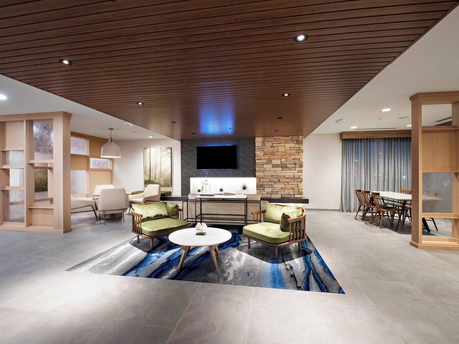 A spacious living area with a modern design, featuring a flat-screen TV, a dining table with chairs, and a coffee table.