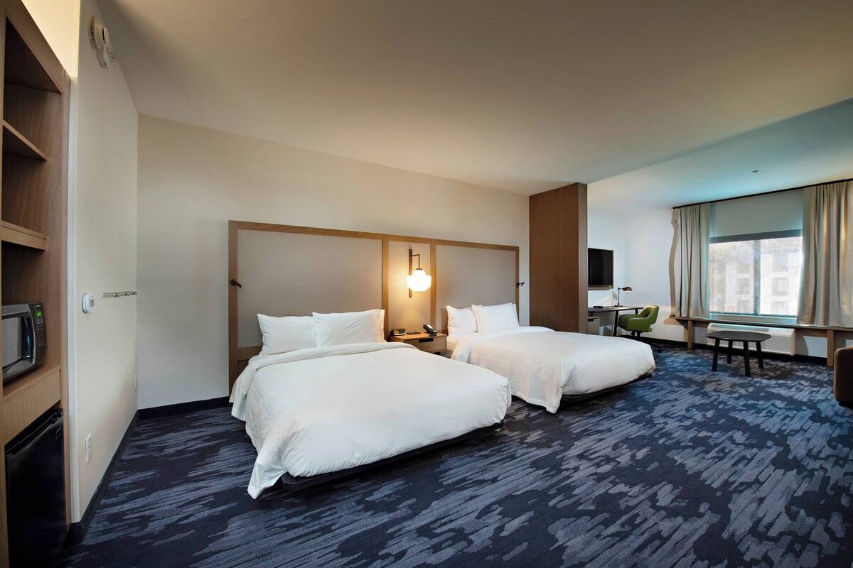 Une chambre d’hôtel avec deux lits, un bureau, une chaise, une télévision et une fenêtre avec des rideaux.