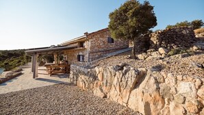 Una casa de piedra con un patio, un banco de madera y un árbol.