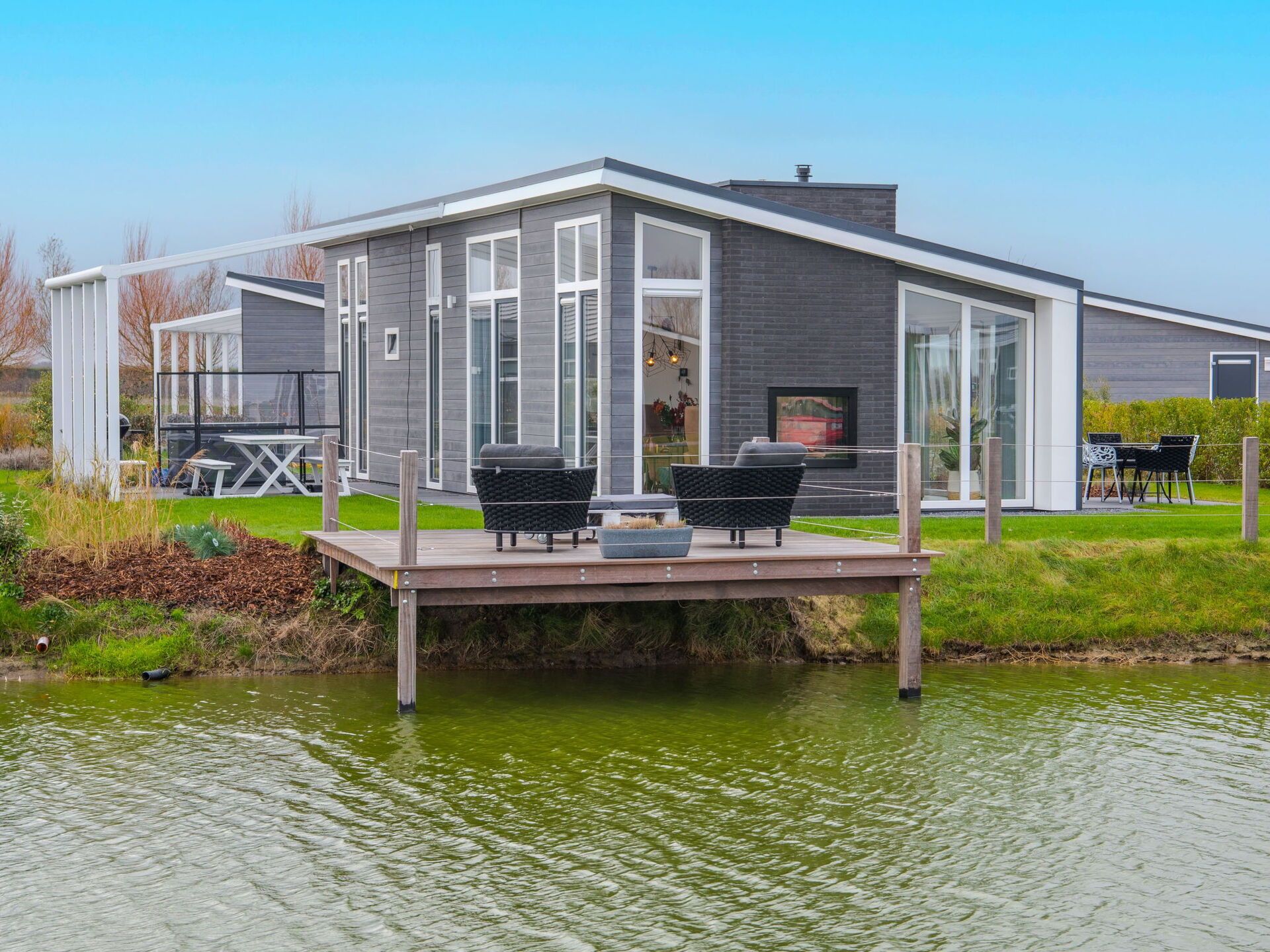 A modern house with a deck over water, featuring a patio with outdoor furniture.