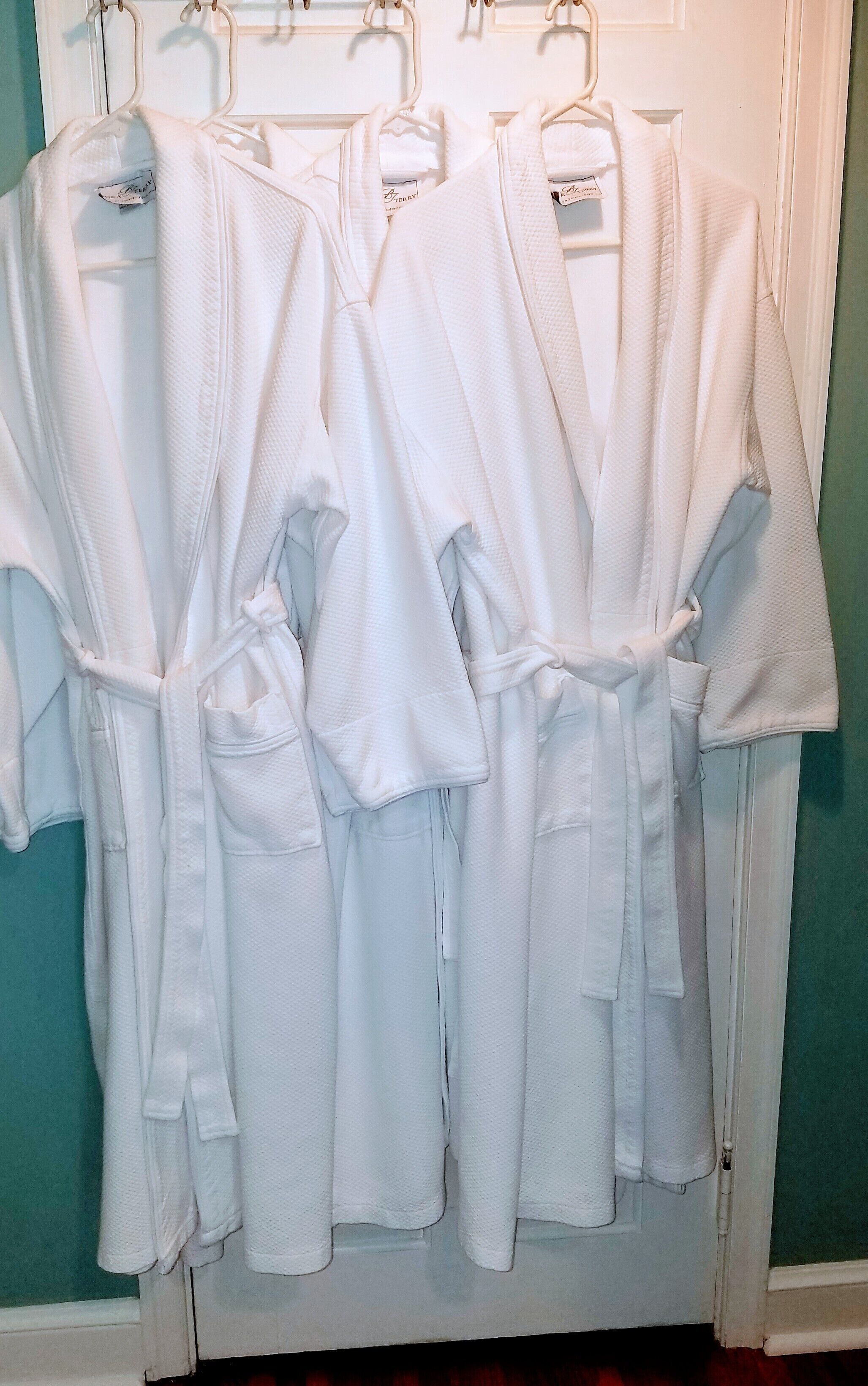 A row of white bathrobes hanging on a door.