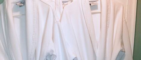 A row of white bathrobes hanging on a door.