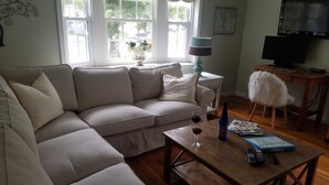 Een woonkamer met een beige bank, een houten salontafel met een wijnglas en een fles, een lamp en een televisie op een meubel.