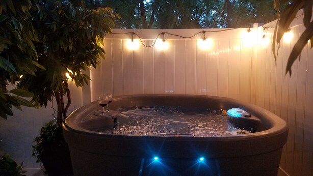Een hottub gevuld met water, omringd door een houten omheining en lichtslingers.