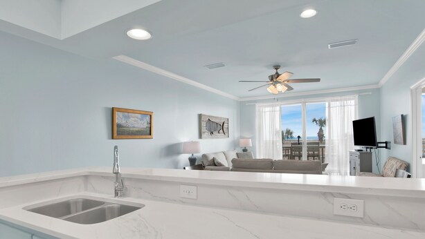 A modern kitchen with a large island, a built-in sink, and a ceiling fan.