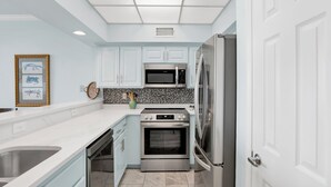 A modern kitchen with light blue cabinets, stainless steel appliances, and a white countertop.