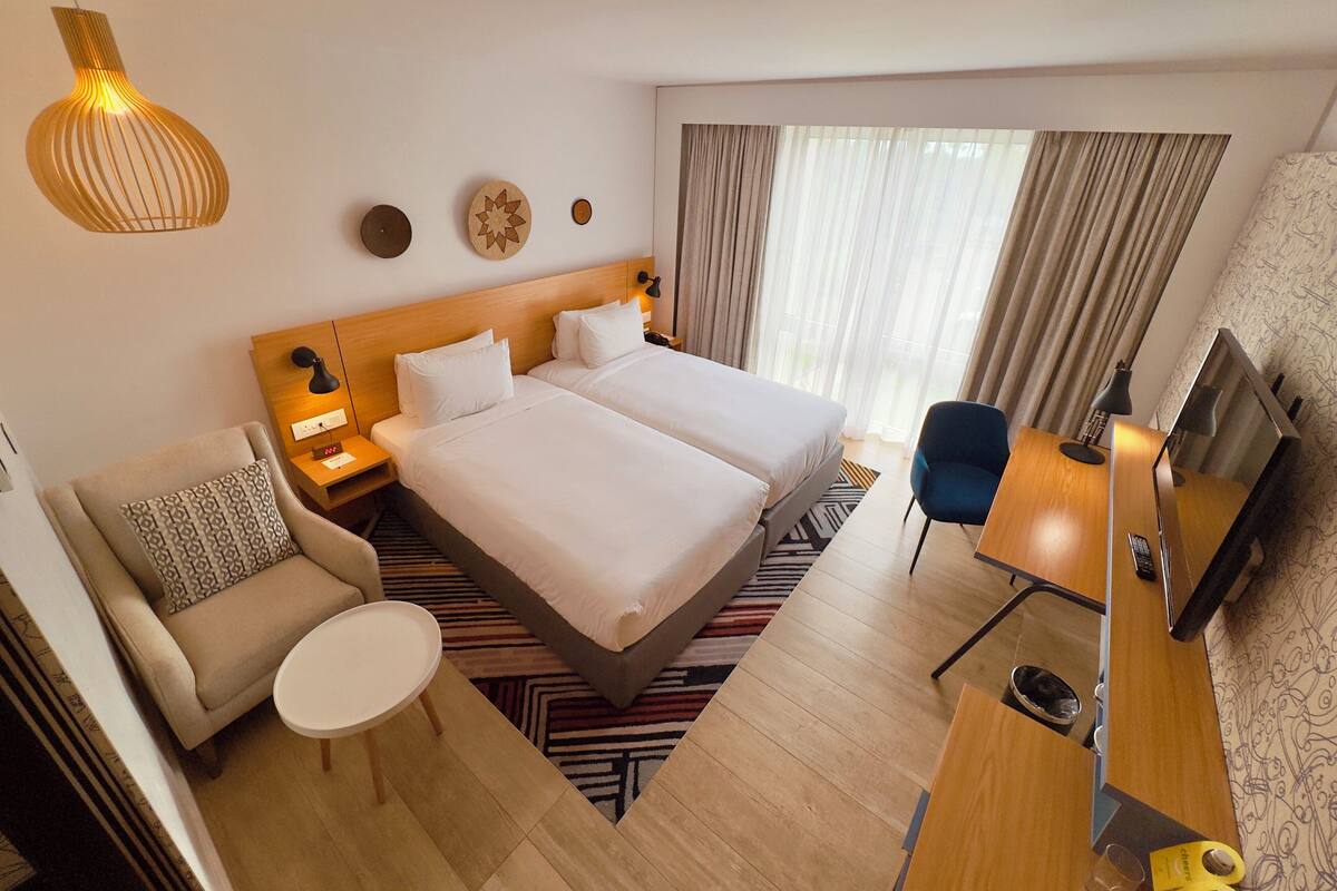 Una camera d'albergo con due letti, una scrivania, una sedia, una televisione e una lampada.