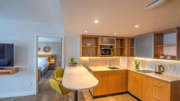 Ett modernt kök med träskåp, en vit bänkskiva och inbyggda vitvaror. Det finns en matplats med ett bord och stolar, och ett sovrum syns i bakgrunden.