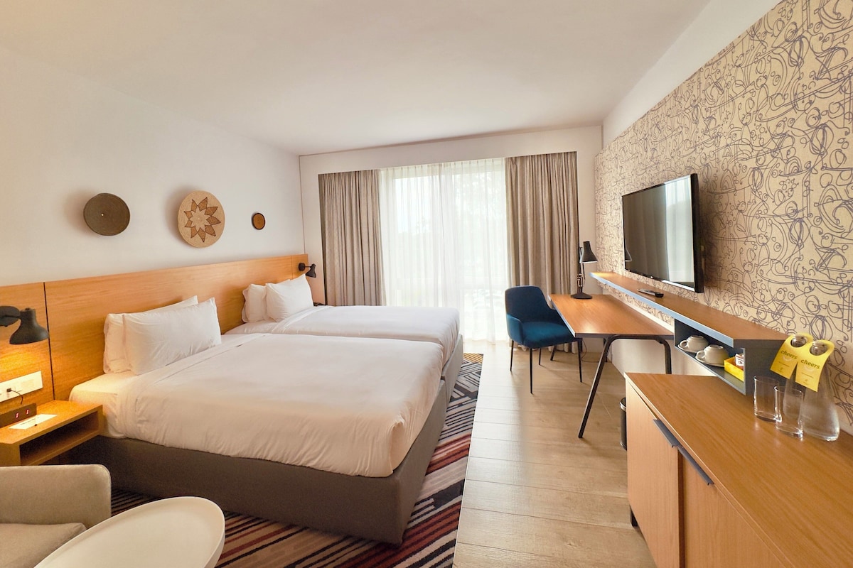 Une chambre d’hôtel avec deux lits, un bureau, une chaise, une télévision et un mur décoré d’un motif.