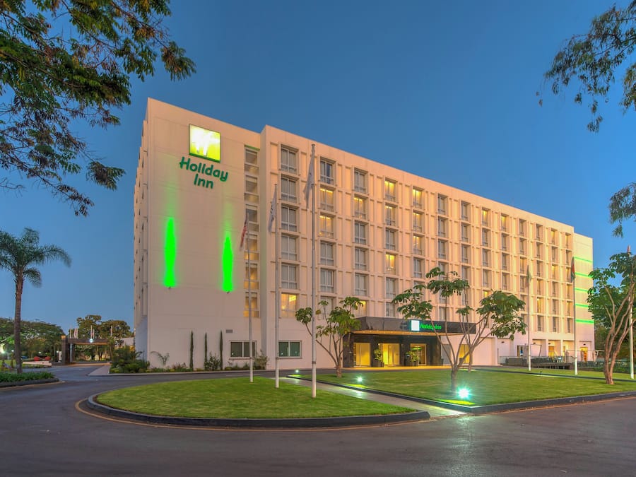 A Holiday Inn hotel with a modern facade, a well-maintained lawn, and a clear sky.