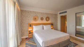 Une chambre d’hôtel avec un grand lit, un mur décoré d’un motif, un miroir et une porte donnant sur une autre pièce.