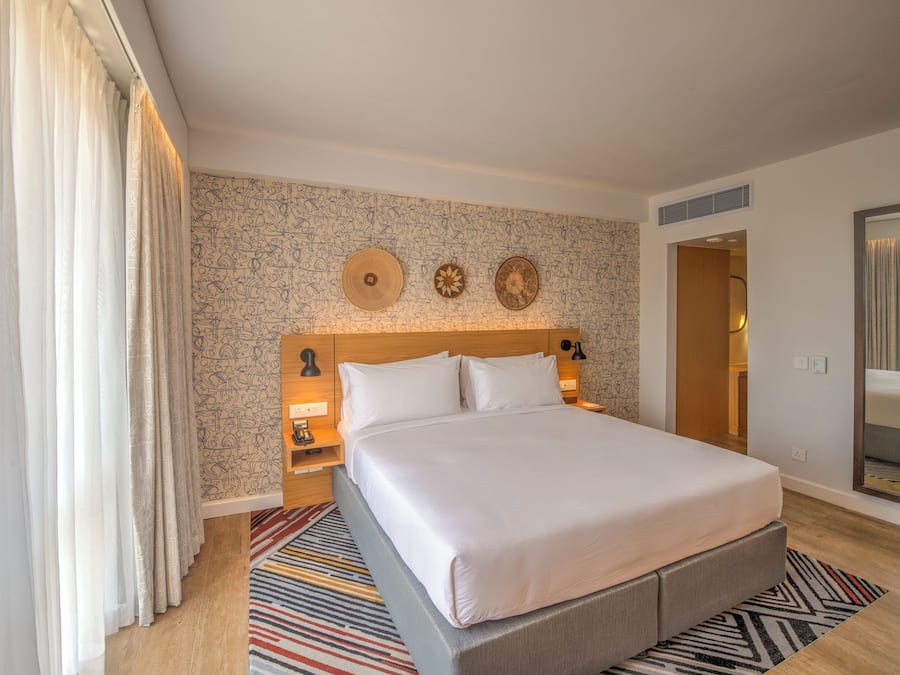 Une chambre d’hôtel avec un grand lit, un mur décoré d’un motif, un miroir et une porte donnant sur une autre pièce.