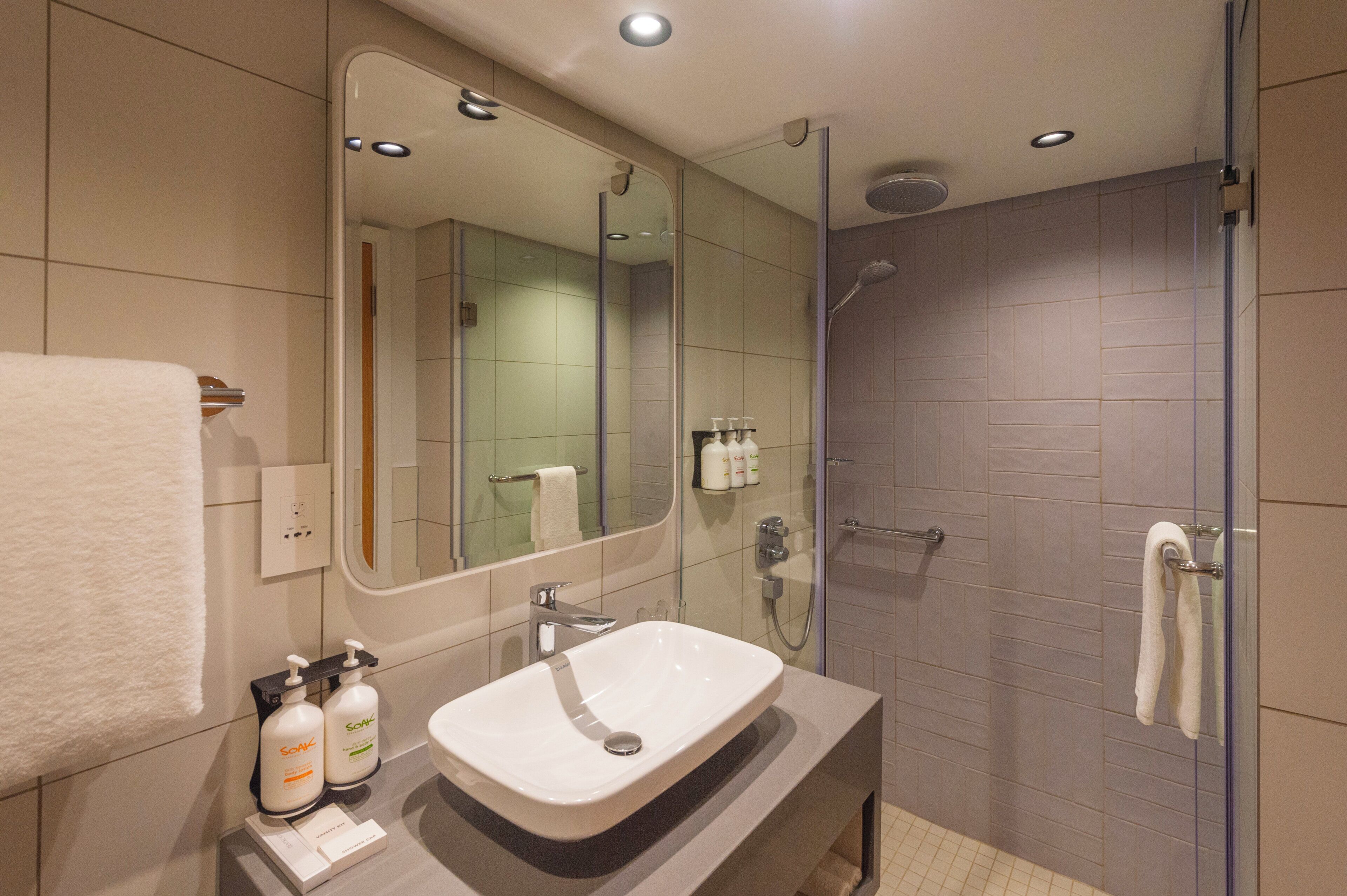 A modern bathroom with a large mirror, a sink, and a glass-enclosed shower.
