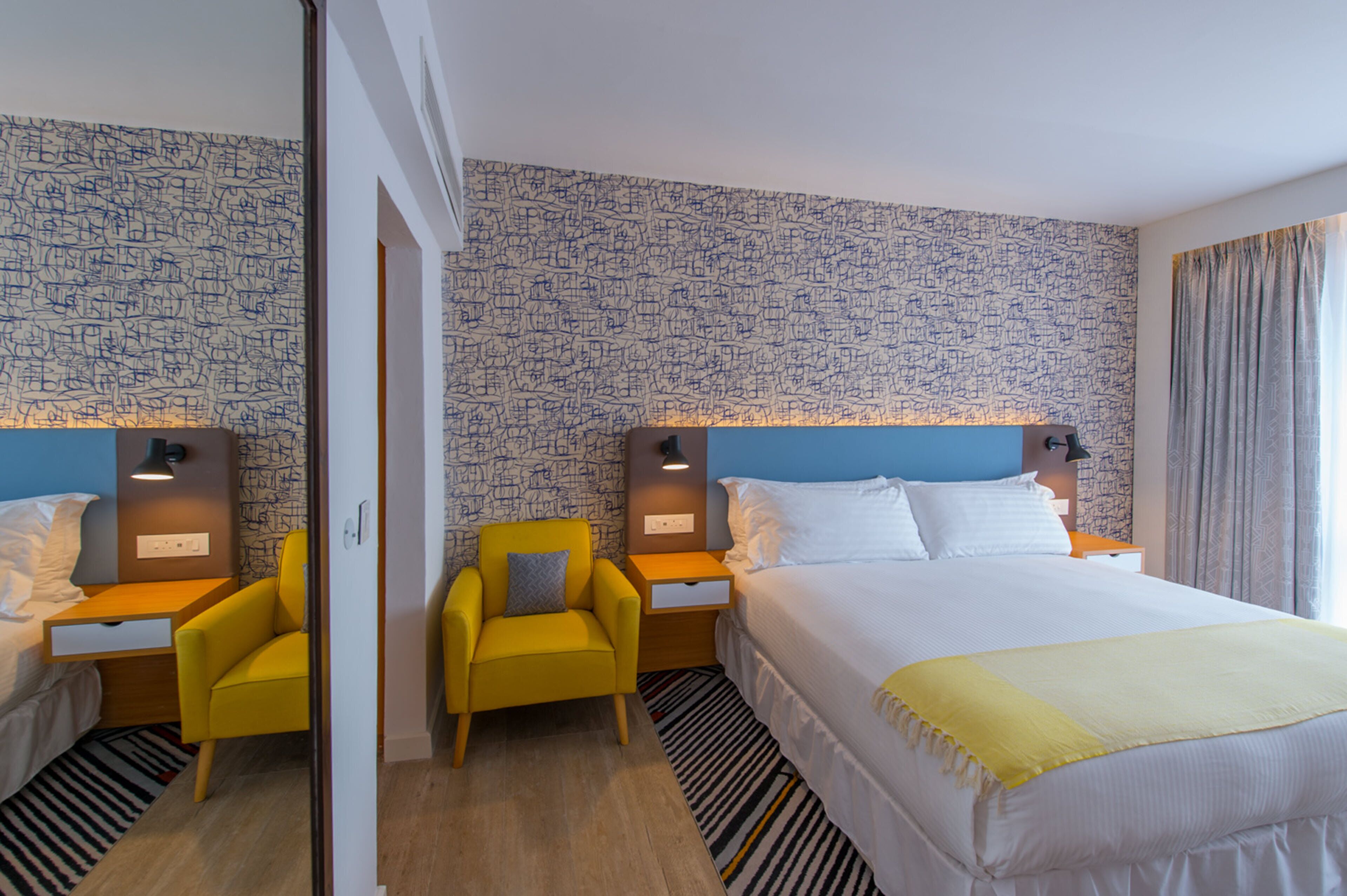 Ein Hotelzimmer mit einem großen Bett, zwei Nachttischen, einem gelben Sessel und raumhoher Tapete.