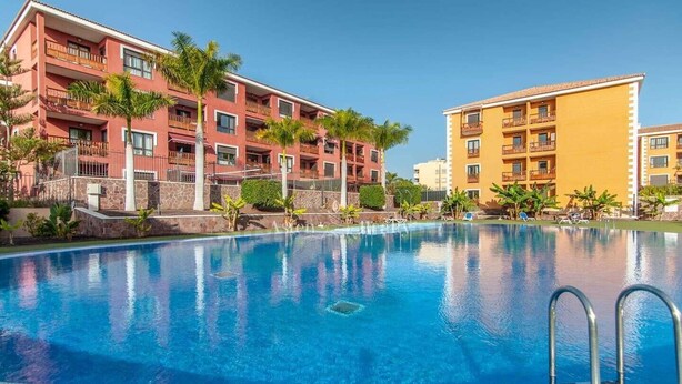A swimming pool with a clear blue water surface, surrounded by a poolside area with lounge chairs and a stone wall.