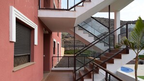 A multi-level residential building with a staircase, a balcony, and a view of a hilly landscape.