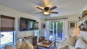 Una sala de estar con ventilador de techo, televisor de pantalla plana, sofá, mesa de centro y vistas al exterior.