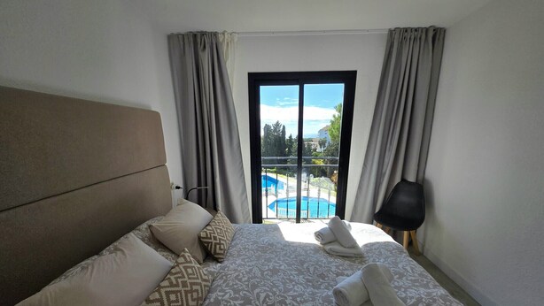 Habitación de hotel con una cama grande, vistas a una piscina y un balcón.
