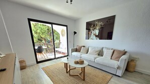 Una sala de estar moderna con un sofá blanco, una mesa de centro y un amplio ventanal corredero que da a un patio exterior.