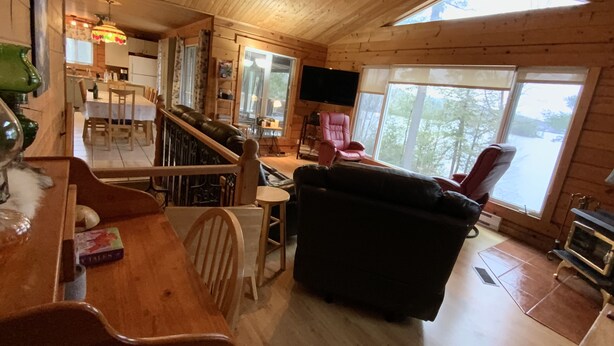 A cozy cabin interior with a wooden dining area, a black sofa, and a television.