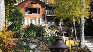 A two-story wooden house with a stone foundation, a balcony, and a stone wall.